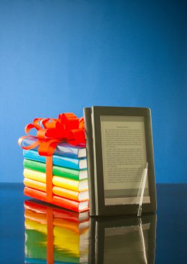 Stack of books with electronic book reader against blue background clipart