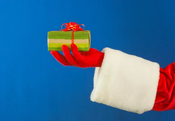 Санта-руки, що тримає подарунок на синьому фоні — стокове фото