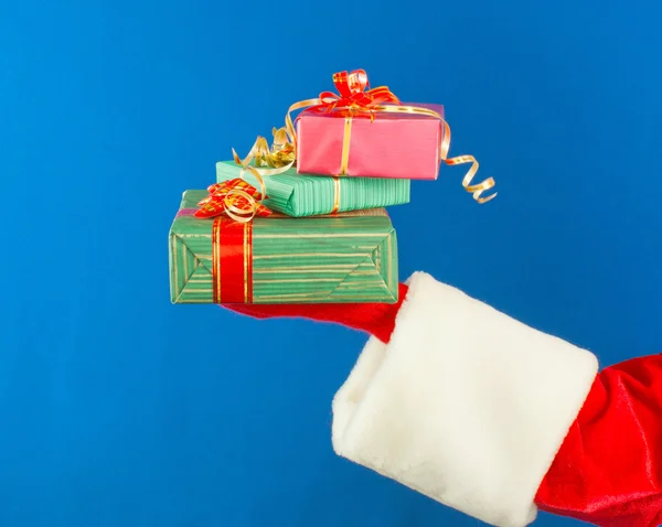 La mano de Santa sostiene regalos sobre fondo azul — Foto de Stock