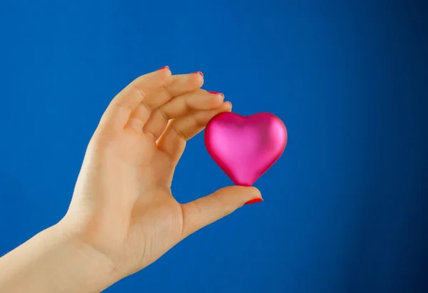 Рука держит подарок в форме сердца на синем фоне — стоковое фото