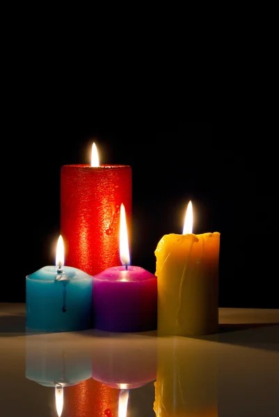 Quatro velas coloridas acesas contra fundo preto — Fotografia de Stock