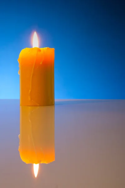 Burning yellow candle against blue background — Stock Photo, Image
