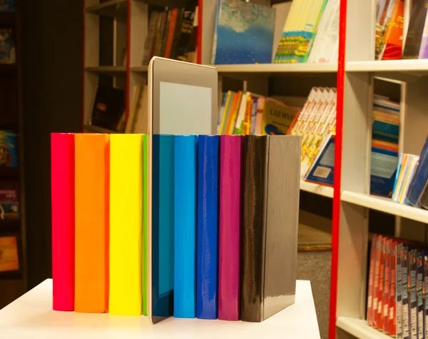 Row of colorful books and tablet PC reader in the book shop