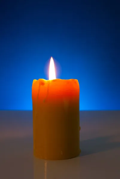 Bruciare candela gialla contro sfondo blu — Foto Stock