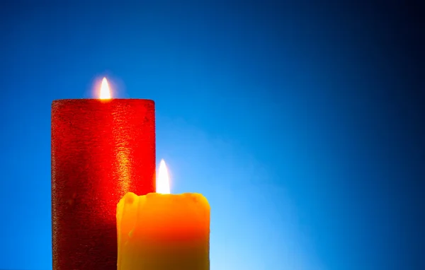 Dvě hořící barevné svíčky na modrém pozadí — Stock fotografie