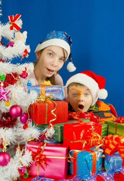 Dos niños sorprendidos mirando detrás de los regalos de Navidad — Foto de Stock