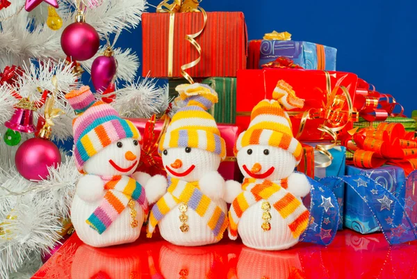 Três bonecos de neve na frente dos presentes de Natal sobre o b azul — Fotografia de Stock