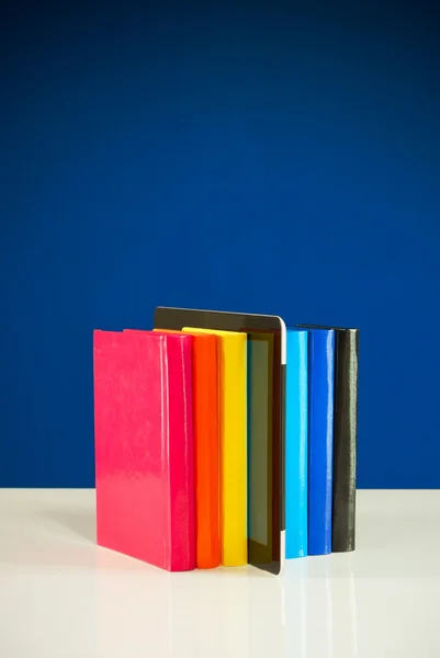 Fila de livros coloridos e tablet PC sobre fundo azul — Fotografia de Stock