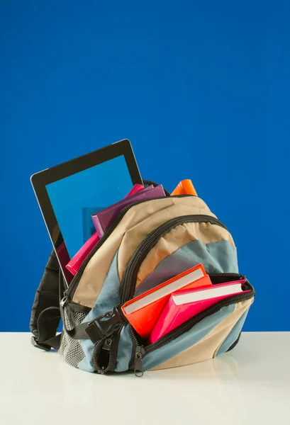 Rucksack mit bunten Büchern und Tablet-PC auf blauem Hintergrund — Stockfoto