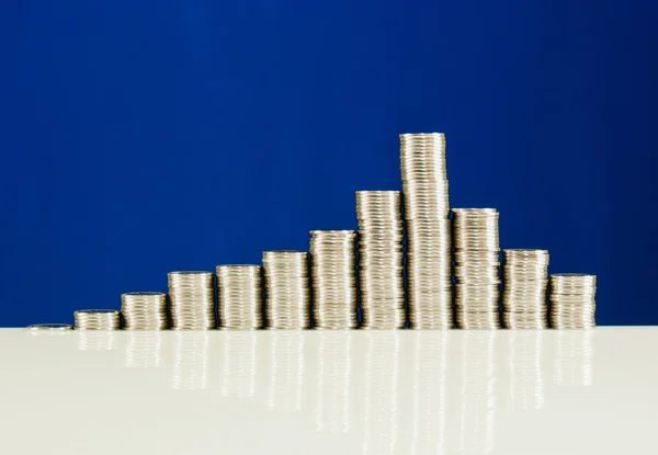 Monedas apiladas en barras sobre fondo azul —  Fotos de Stock