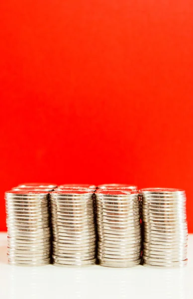 Mynt staplade i barer mot röd bakgrund — Stockfoto