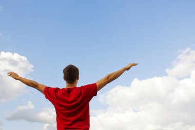 Young man staying with raised hands against blue sky clipart