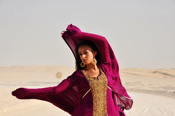 可爱的年轻女人在阿拉伯沙漠穿紫色东方服饰 免版税图库图片