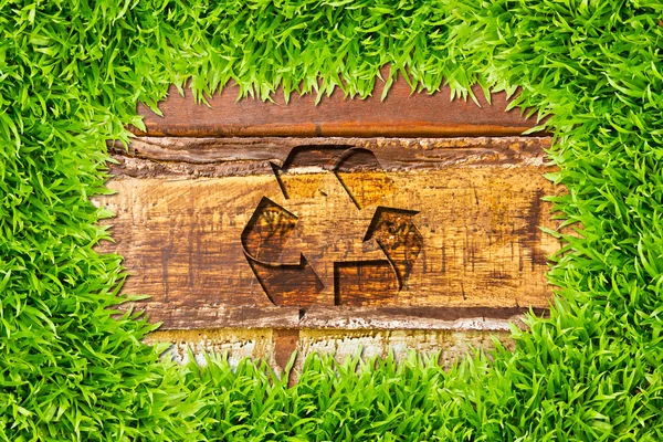 Grönt gräs och återvinna underteckna på trä bakgrund — Stockfoto