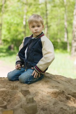 A little boy builds a sand castle. clipart