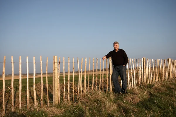 A mature man standing against a fence — Stock Photo, Image