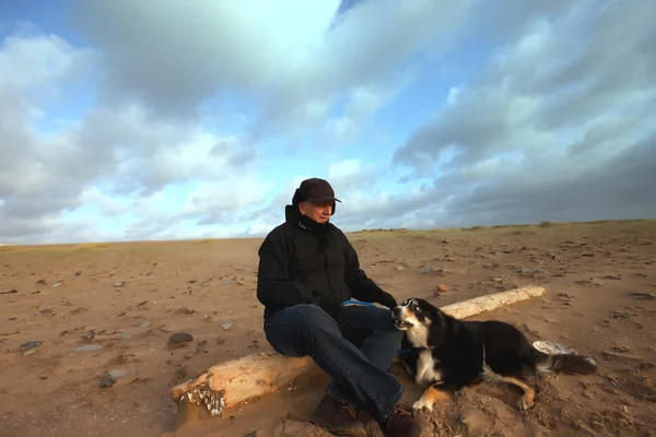 Un uomo e il suo cane seduti su un tronco — Foto Stock