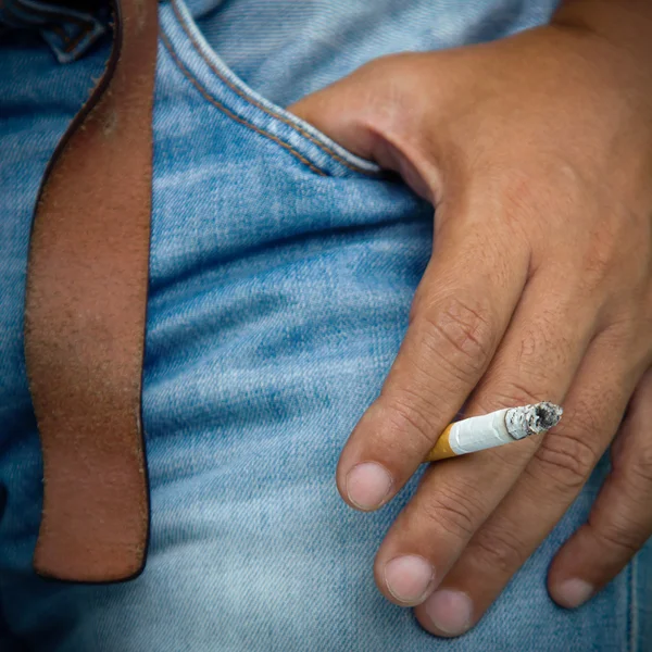 Сигарета крупным планом в мужской руке на старом джинне — стоковое фото