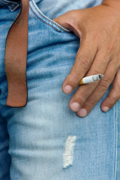 Сигарета крупным планом в мужской руке на старом джинне — стоковое фото