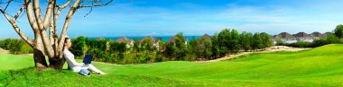 Pretty woman sitting with laptop under tree. Beautiful panoramic view of idyllic landscape clipart