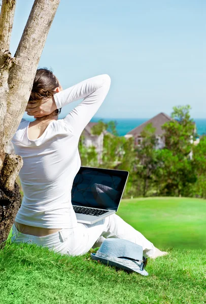 Ładna kobieta siedzi przez drzewo z laptopa — Zdjęcie stockowe