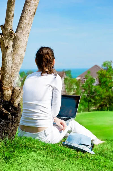 Молода жінка сидить під деревом з ноутбуком і мріє. Idyllic відкриті пейзажі — стокове фото