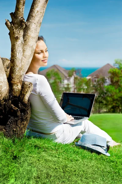 Mujer bonita sentada junto al árbol con ordenador portátil —  Fotos de Stock