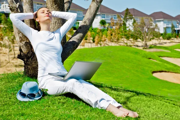 Bella femmina seduta sotto un albero con computer portatile il giorno d'estate — Foto Stock