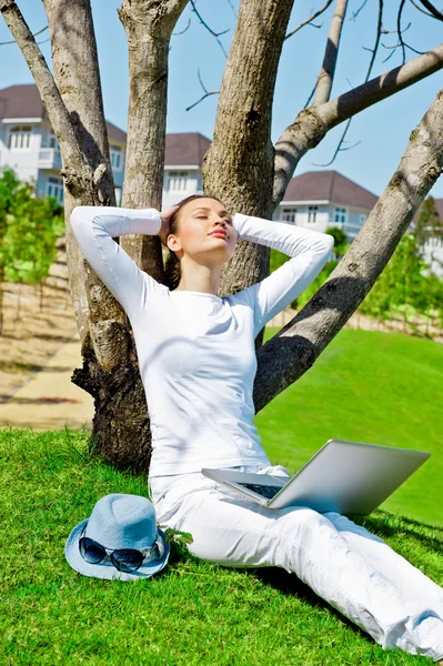 Csinos női ül egy laptop fa alatt a nyári nap — Stock Fotó