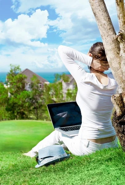 Ung kvinna sitter under träd med laptop och drömmer. idylliska utomhus landskap — Stockfoto