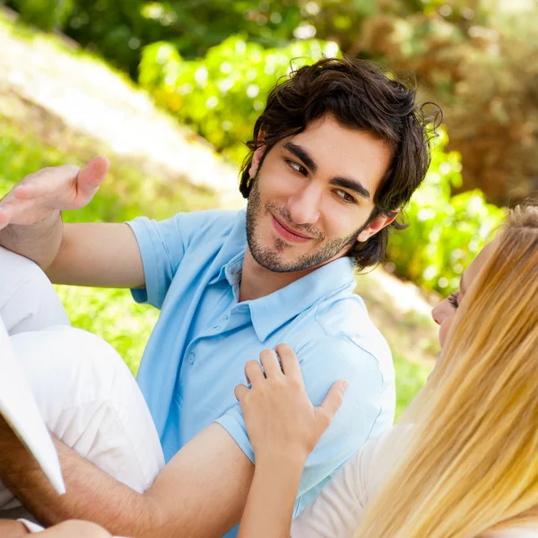 Feliz pareja de estudiantes con un cuaderno sentado en la hierba en cam —  Fotos de Stock