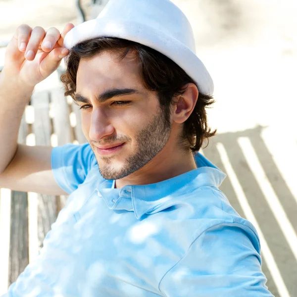 Portrait of a handsome young man sitting in the sun on bench at — Stock Photo, Image