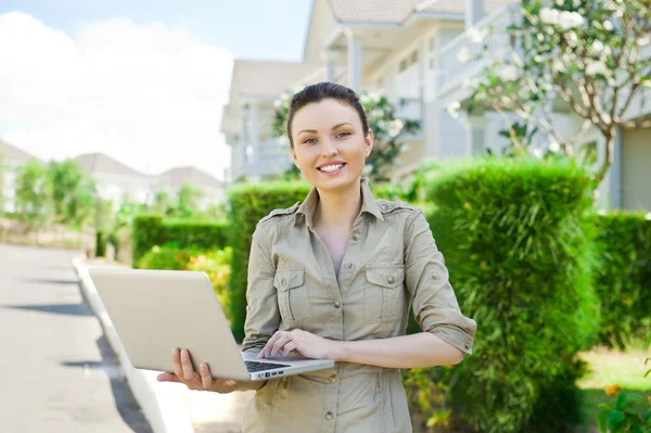 Ung affärskvinna (fastighetsmäklare) innehar en laptop och presentera fristående enfamiljshus — Stockfoto