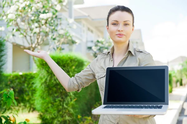 Молодая предпринимательница (агент по недвижимости) держит в руках ноутбук и представляет отдельный семейный дом — стоковое фото