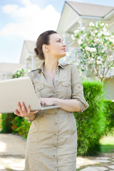 Jeune jolie agent immobilier féminin avec ordinateur portable présentant belle maison individuelle — Photo