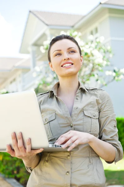 Jeune jolie agent immobilier féminin avec ordinateur portable présentant belle maison individuelle — Photo
