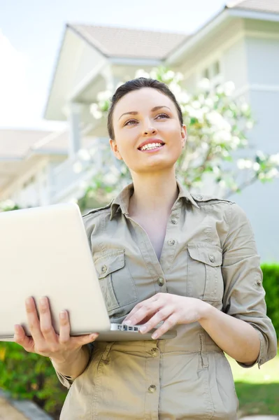 stock image Young pretty female realty agent with laptop presenting beautiful detached house