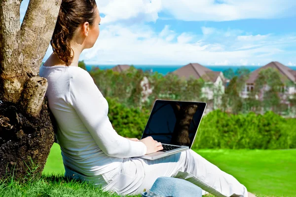 Mujer joven sentada bajo el árbol con portátil y soñando. Idílico paisaje al aire libre —  Fotos de Stock