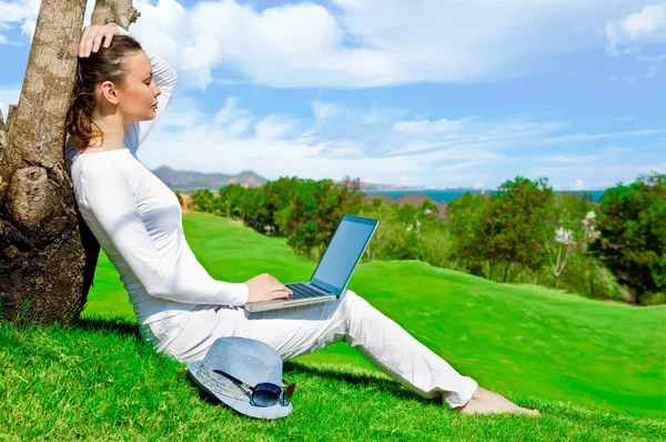 Hübsche Frau sitzt mit Laptop am Baum — Stockfoto