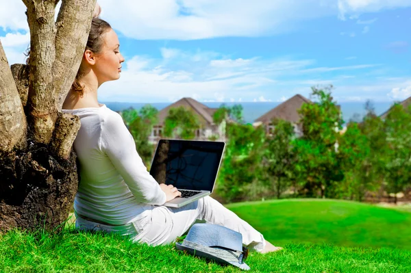 Junge Frau sitzt unter Baum mit Laptop und träumt. idyllische Outdoor-Landschaft — Stockfoto