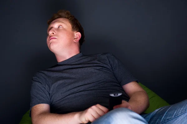Portrait of a young man watching TV alone with a remote control — Stock Photo, Image