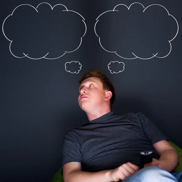 Portrait of a young man watching TV alone with a remote control and dreaming — Stock Photo, Image