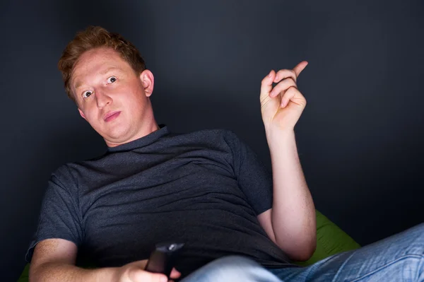 Porträtt av en ung man tittar på tv ensam med en fjärrkontroll — Stockfoto