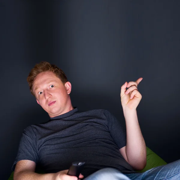 Portrait of a young man watching TV alone with a remote control — Stock Photo, Image