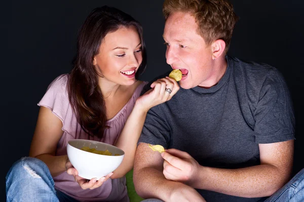 Casal feliz sentados juntos assistindo algo interessante na televisão e comer - fundo cinza — Fotografia de Stock