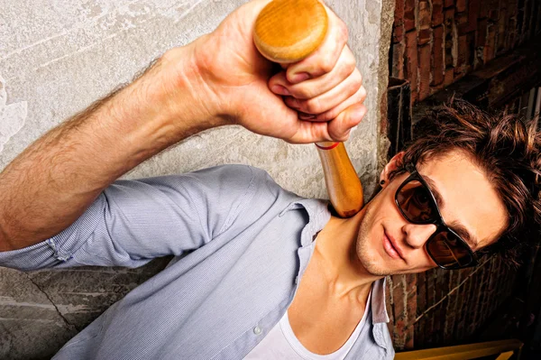 Portrait of young guy with bat leaning on the wall — Stock Photo, Image