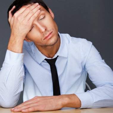 Bored businesspeople: man sitting at desk holding his head. Youn clipart