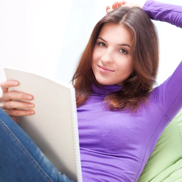 Jovem mulher adulta escrevendo em seu livro enquanto sentada em um lar — Fotografia de Stock