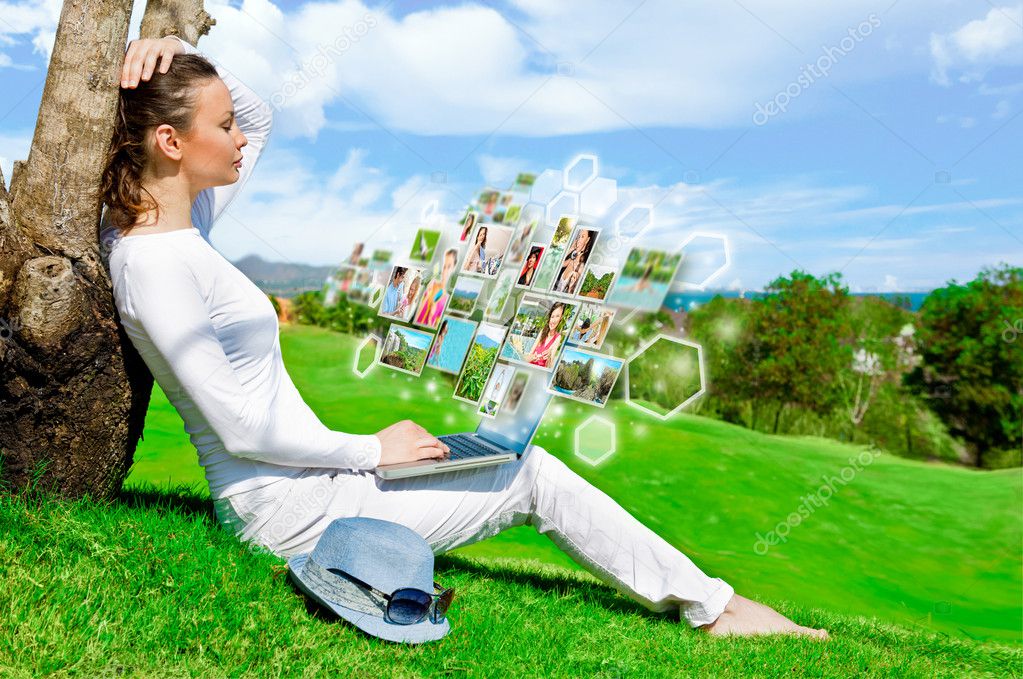 Pretty woman sitting by tree with laptop computer