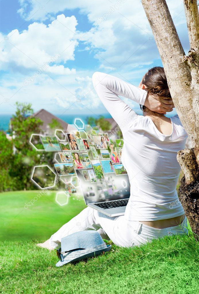 Young woman sitting under tree with laptop and dreaming. Idyllic